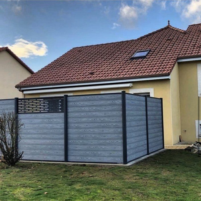 Clôture composite grise à poteaux anthracite au fond d'un jardin